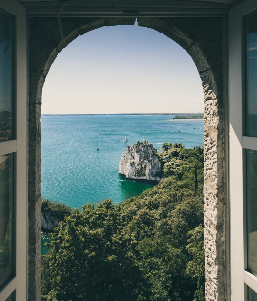 Panoramic Italian landscape framed by the window: rolling hills kissed by sunlight, dotted with rustic villas and cypress trees, under a serene blue sky.